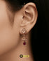 Close-up of a model wearing elegant rose gold zircon huggie earrings with a floral jhumka design and red teardrop stone.