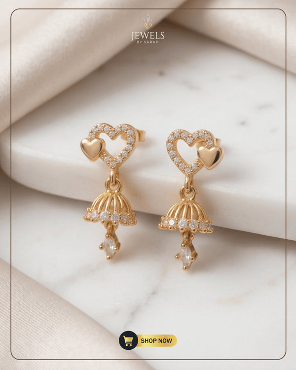 Pair of gold-plated dual heart jhumka earrings with Zircon accents on a white marble surface.