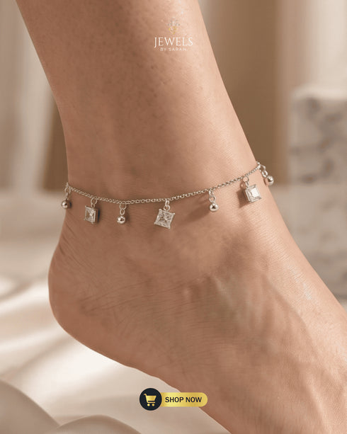 Close-up of a model's ankle wearing a shimmering square Zircon charm anklet in silver.