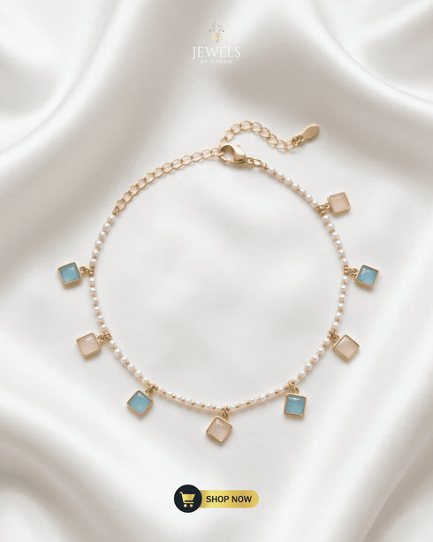 Gold-plated pearl anklet with alternating sky blue and white square gemstone charms on a white silk background.