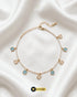 Gold-plated pearl anklet with alternating sky blue and white square gemstone charms on a white silk background.