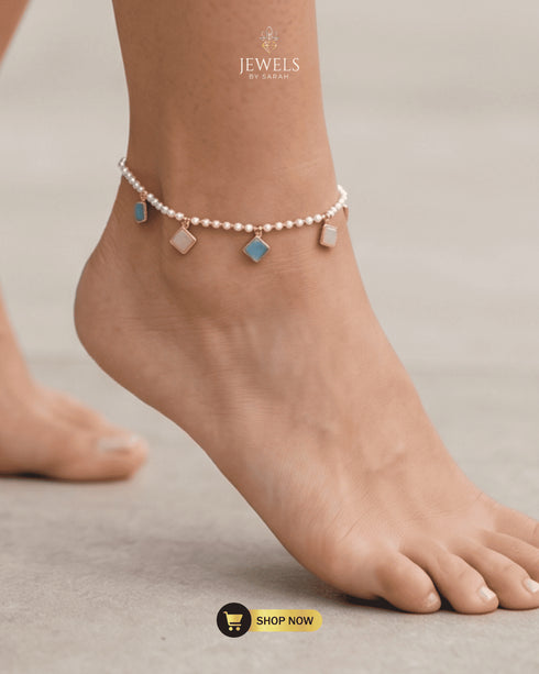 Close-up of a model wearing an elegant pearl and pastel gemstone anklet on a bare foot.