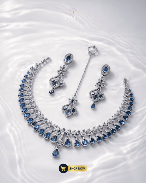 Top view of silver zircon and blue stone necklace set displayed on a shimmering water-ripple background.