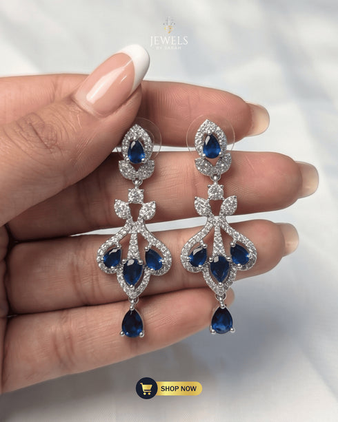 Close-up of silver zircon chandelier earrings with teardrop blue sapphire stones held by hand.