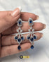 Close-up of silver zircon chandelier earrings with teardrop blue sapphire stones held by hand.