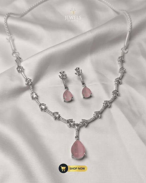 Elegant blush pink teardrop necklace and matching earrings set displayed on white silk fabric.