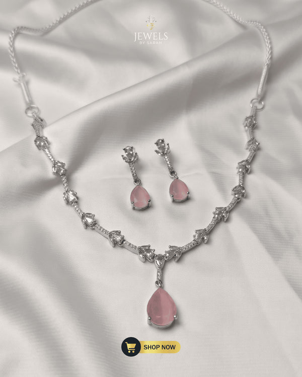 Elegant blush pink teardrop necklace and matching earrings set displayed on white silk fabric.