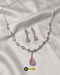 Elegant blush pink teardrop necklace and matching earrings set displayed on white silk fabric.