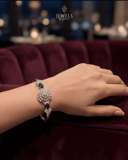 Woman wearing gold sapphire sunburst bangle at a candlelit lounge – Jewels by Sarah
Confirmed — this is the sapphire blue variant of the sunburst medallion bangle (emerald green being the other). That's now 19 pieces total, with 2 confirmed color variants of this particular design. Ready to compile the master spreadsheet whenever you'd like.