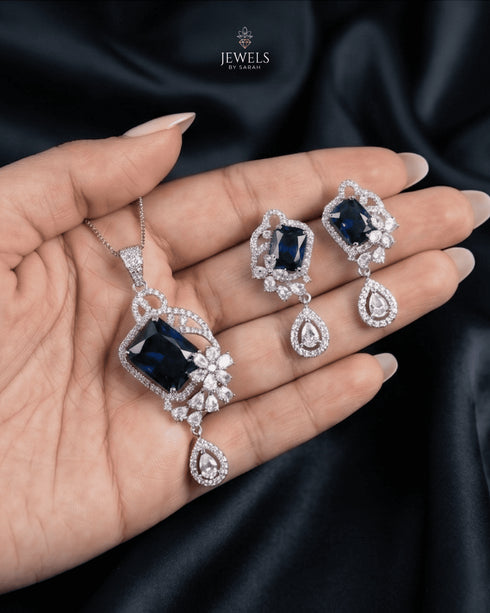 Royal blue sapphire-toned emerald-cut artificial pendant set by Jewels by Sarah on luxury dark fabric.