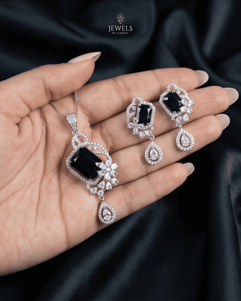 et black luxury emerald-cut gemstone pendant with a simple minimalist chain held against dark silk fabric.