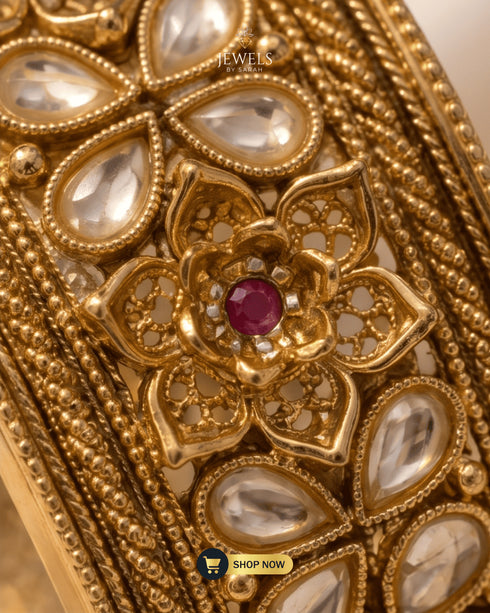 Macro detail of ruby zircon center and clear AD stone petals on a wide gold bangle.