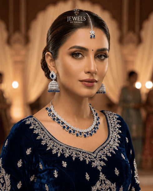 "Model wearing sapphire blue jhumka necklace set with tikka and earrings styled with navy velvet outfit"