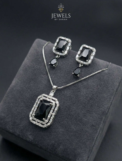 Elegant black onyx color jewelry set with emerald-cut pendant and drop earrings on grey velvet box.