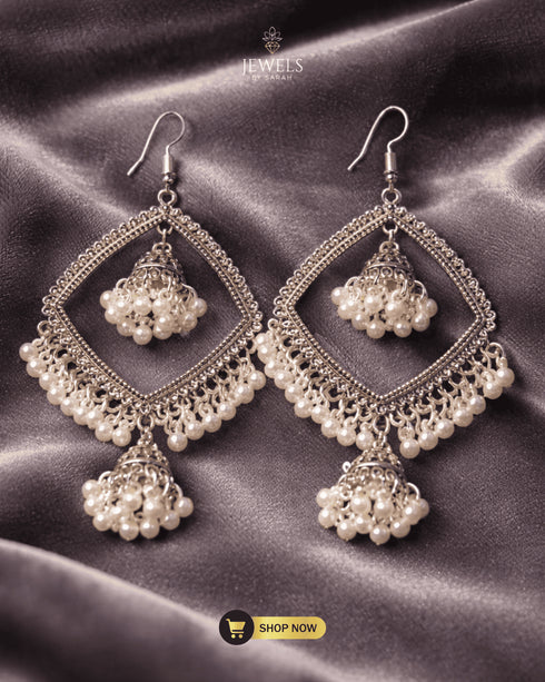 Traditional antique silver jhumka earrings with white pearls on a grey velvet background.