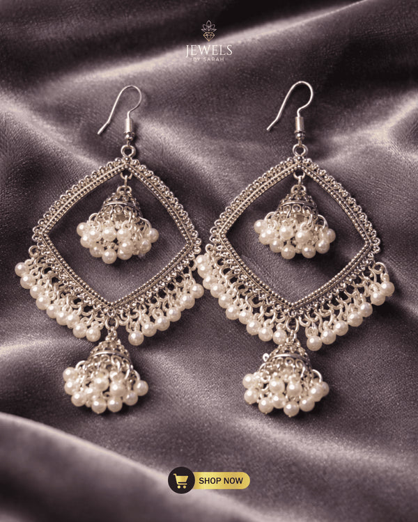 Traditional antique silver jhumka earrings with white pearls on a grey velvet background.