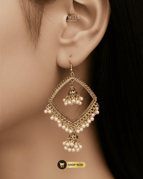 Close-up of a model wearing traditional gold-plated geometric earrings with hanging pearl jhumkas.