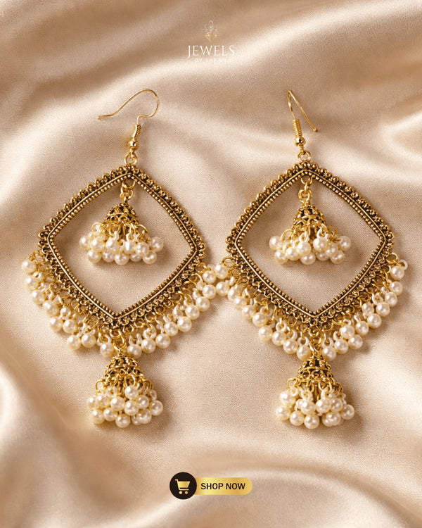 Pair of antique gold-plated jhumka earrings with white pearls on a shimmering gold silk background.
