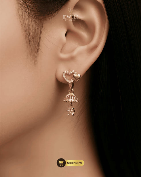 Close-up of a model wearing elegant gold-plated heart-shaped jhumka earrings with a crystal drop.