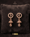 Pair of minimalist rose gold zircon jhumka earrings with leaf motifs on a dark velvet cushion.