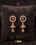 Pair of minimalist rose gold zircon jhumka earrings with leaf motifs on a dark velvet cushion.