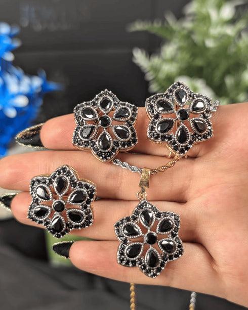 Premium black floral pendant necklace, earrings, and ring displayed on a hand to show scale and detailed craftsmanship.