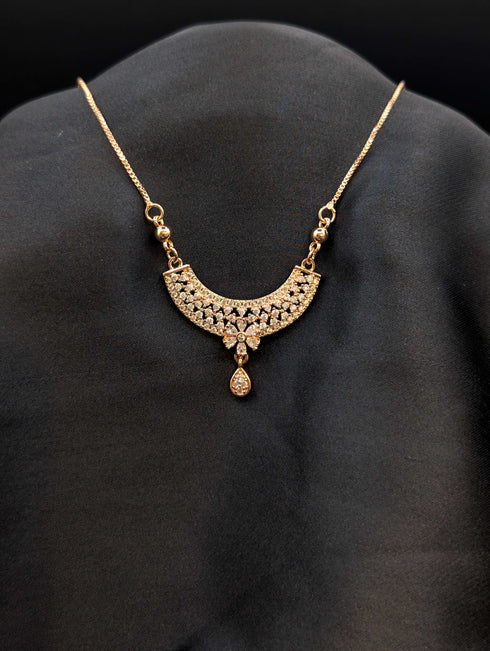 Rose gold filigree crescent necklace with white cubic zirconia floral center and teardrop stone dangle on a dark background.