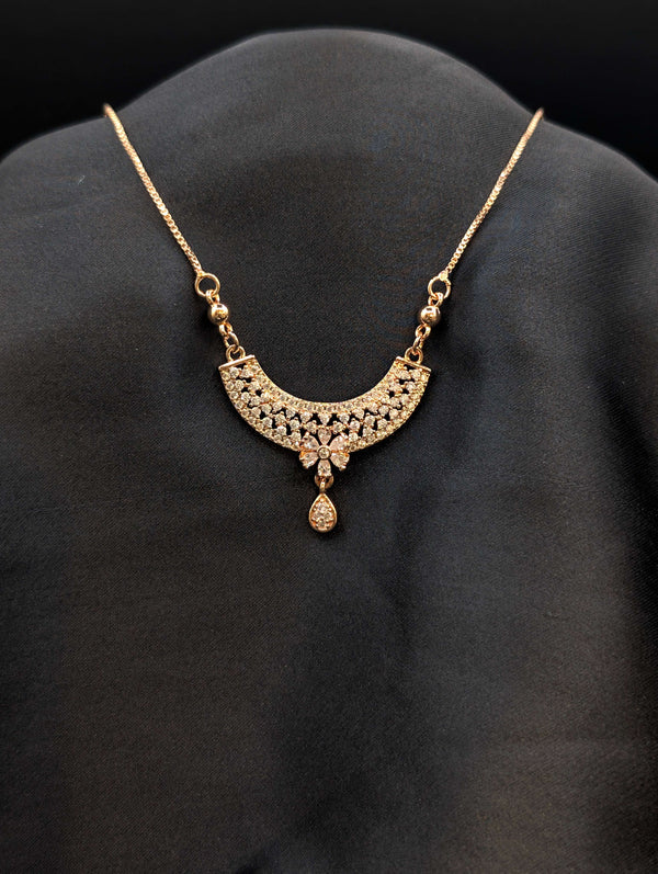 Rose gold filigree crescent necklace with white cubic zirconia floral center and teardrop stone dangle on a dark background.