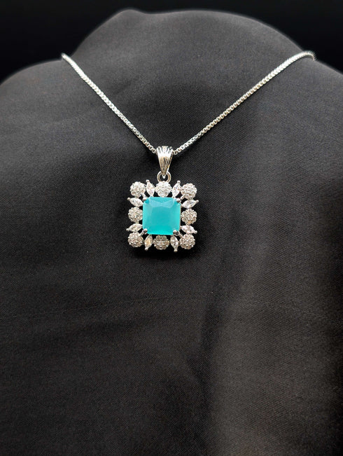Silver-plated necklace with a square seafoam turquoise pendant surrounded by a white stone floral halo on a black fabric display.
