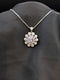 Silver-plated floral medallion necklace with pastel lavender and white cubic zirconia stones in a sunflower pattern on a black background.