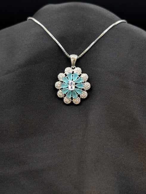 Silver-plated floral medallion necklace with teal blue pear-cut stones and a white cubic zirconia border on a black background.