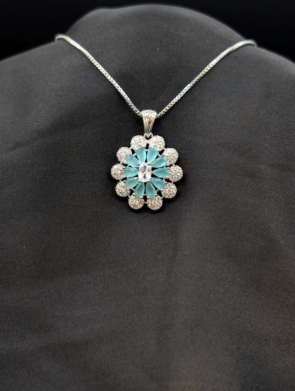 Silver-plated floral medallion necklace with teal blue pear-cut stones and a white cubic zirconia border on a black background.