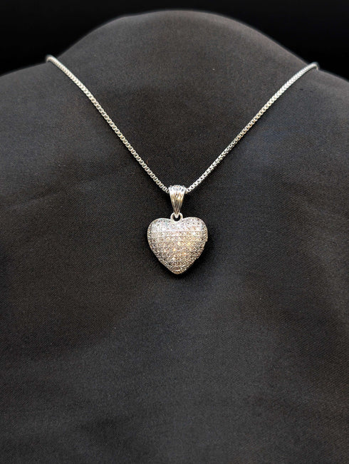 Silver-tone stainless steel heart pendant fully encrusted with white pave cubic zirconia on a box chain against a black background.