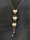 Gold-plated stainless steel lariat necklace featuring three cascading heart charms with pearl inlays and crystal drop accents.