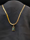 Gold-plated stainless steel herringbone chain necklace with a rectangular emerald green baguette stone pendant against a black background.