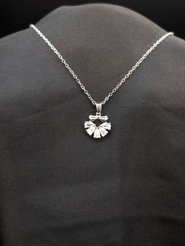 Silver-toned stainless steel necklace featuring a fan-shaped pendant with pear-cut and baguette crystals on a black background.