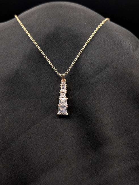 Gold-plated stainless steel necklace with a vertical tiered drop pendant featuring five graduated square-cut crystals on a black background.