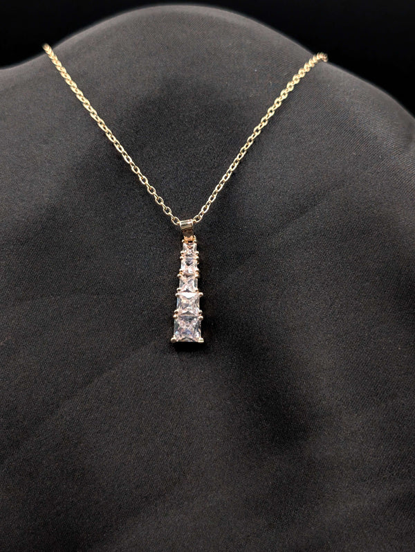 Gold-plated stainless steel necklace with a vertical tiered drop pendant featuring five graduated square-cut crystals on a black background.