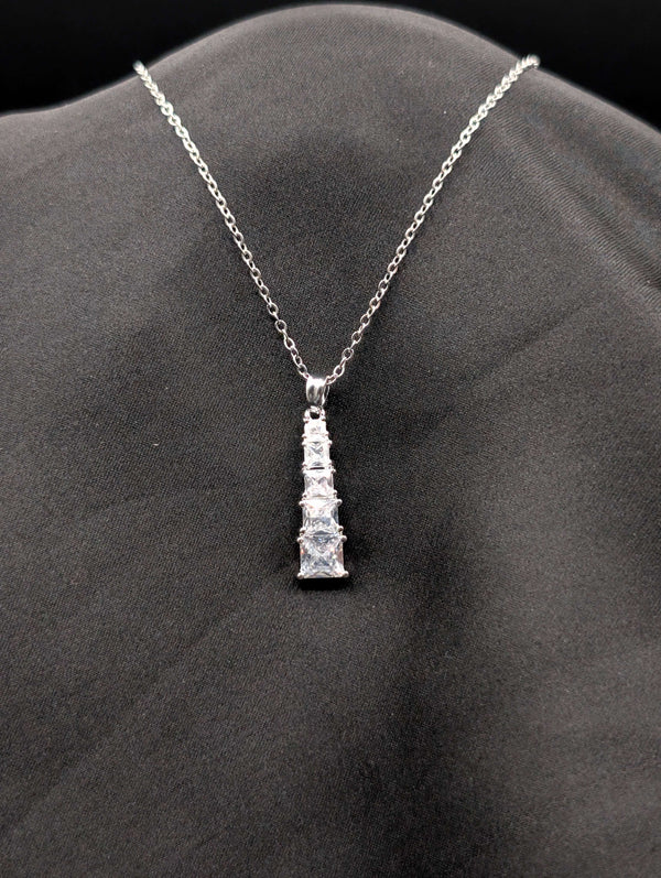 Silver-toned stainless steel necklace with a vertical tiered drop pendant featuring five graduated square-cut crystals on a black background.
