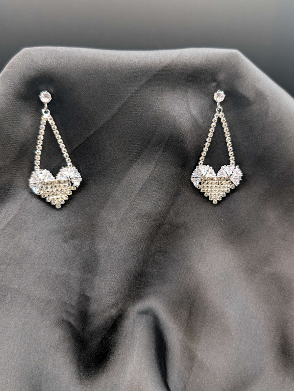 Silver-toned chandelier earrings featuring a cascading crystal design and a pave-encrusted heart pendant on a dark grey background.
