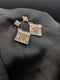 Gold-toned geometric statement earrings with square drop pendants featuring champagne and clear crystal pave on a dark background.