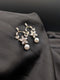 Gold-toned drop earrings featuring a marquise crystal flower blossom design and a white pearl drop on a dark fabric background.
