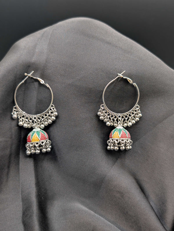 Silver-toned hoop earrings with multi-color enamel Jhumka bells and beaded fringe against a dark grey background.