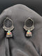 Silver-toned hoop earrings with multi-color enamel Jhumka bells and beaded fringe against a dark grey background.