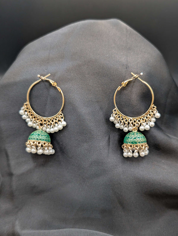 Gold-toned Jhumka hoop earrings with emerald green enamel bell pendants and white pearl fringe on a dark fabric background.