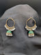 Gold-toned Jhumka hoop earrings with emerald green enamel bell pendants and white pearl fringe on a dark fabric background.