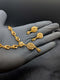 Handheld view of a 24k gold plated necklace with heart-shaped links and matching floral drop earrings against a dark background.