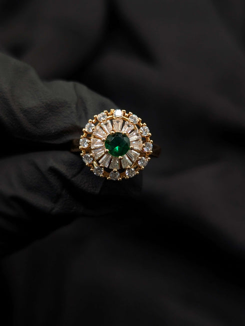 Close-up of a gold Ballerina style ring with a round emerald green center stone and sunburst diamond halo.