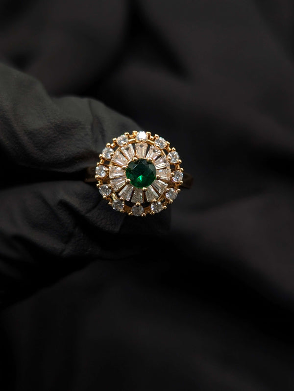 Close-up of a gold Ballerina style ring with a round emerald green center stone and sunburst diamond halo.