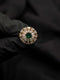 Close-up of a gold Ballerina style ring with a round emerald green center stone and sunburst diamond halo.